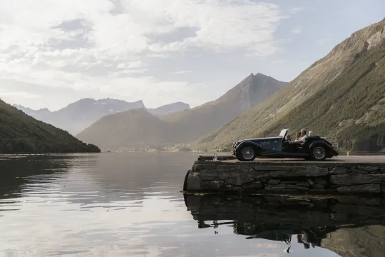 A classic car parked by the water looking into a large fjord