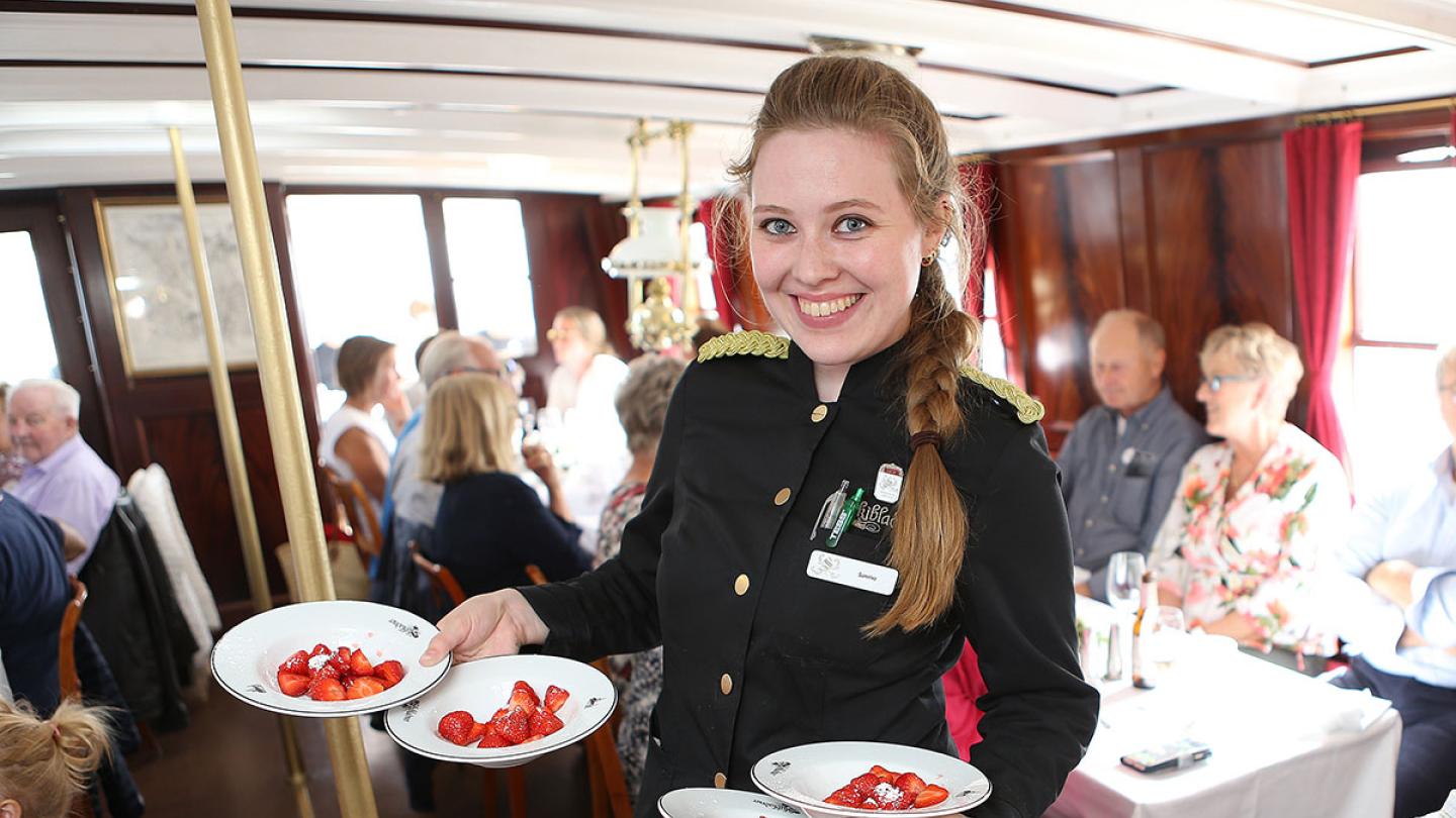 A friendly server serving strawberries onboard Skibladner