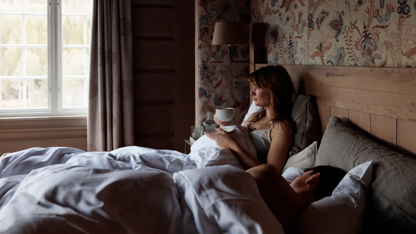 A woman drinking coffee in bed at Storfjord Hotel