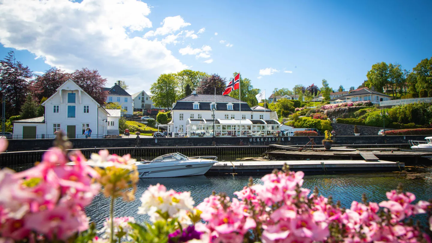 The exterior of Bekkjarvik Gjestgiveri with the harbour in front while the sun is shining