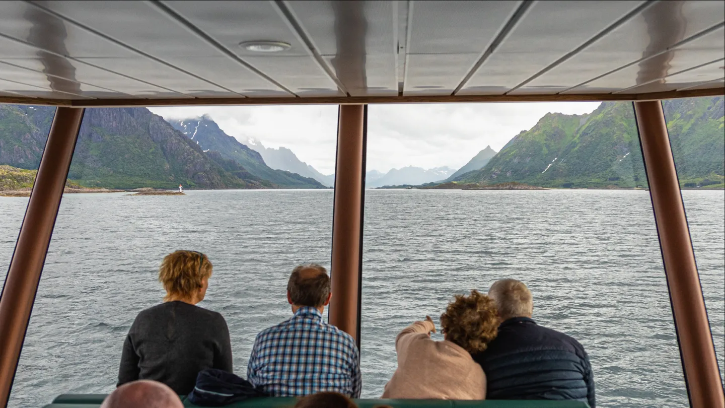 People sitting inside a modern boat while looking out through the windows over Trollfjord
