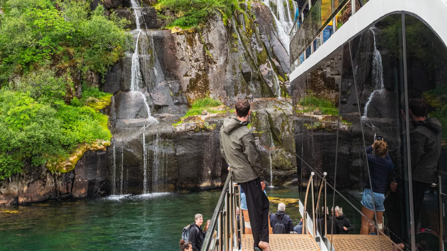 A man leaning against the handrail onboard a modern boat looking at a waterfall in Trollfjord