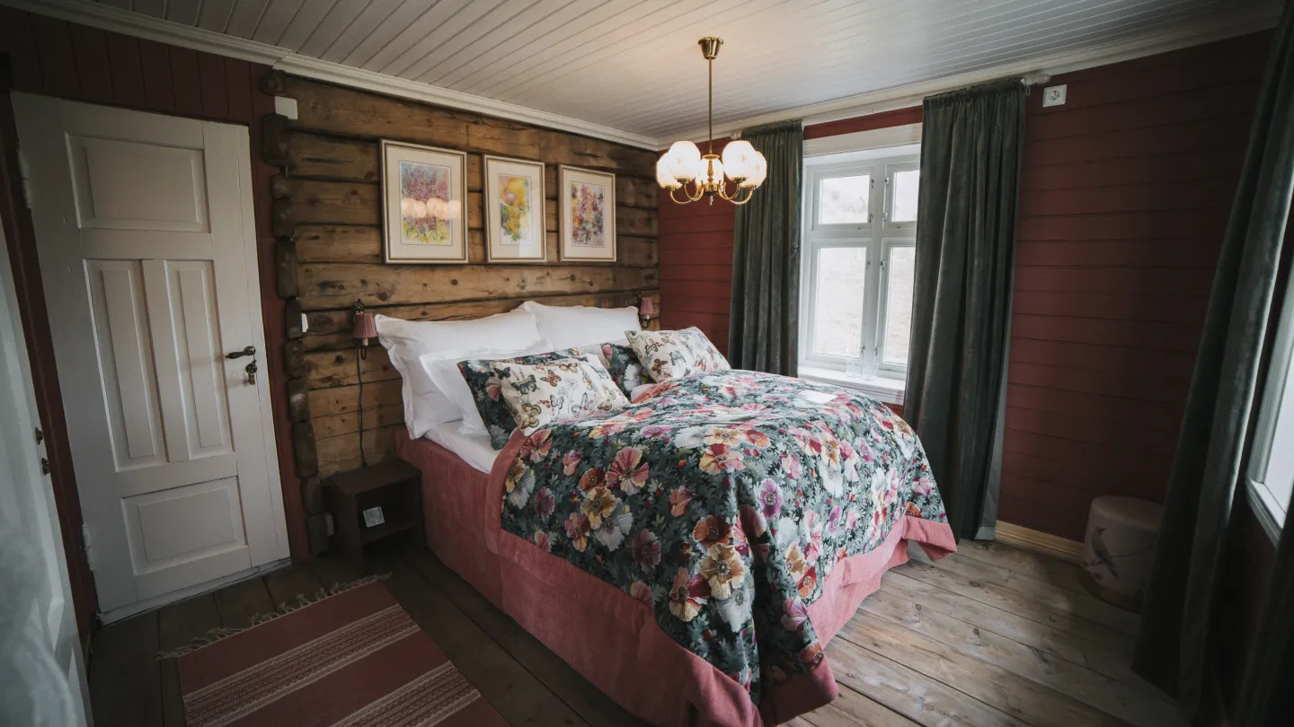 A bed in a room at Flatheim. The walls are painted red, green curtains and white doors.