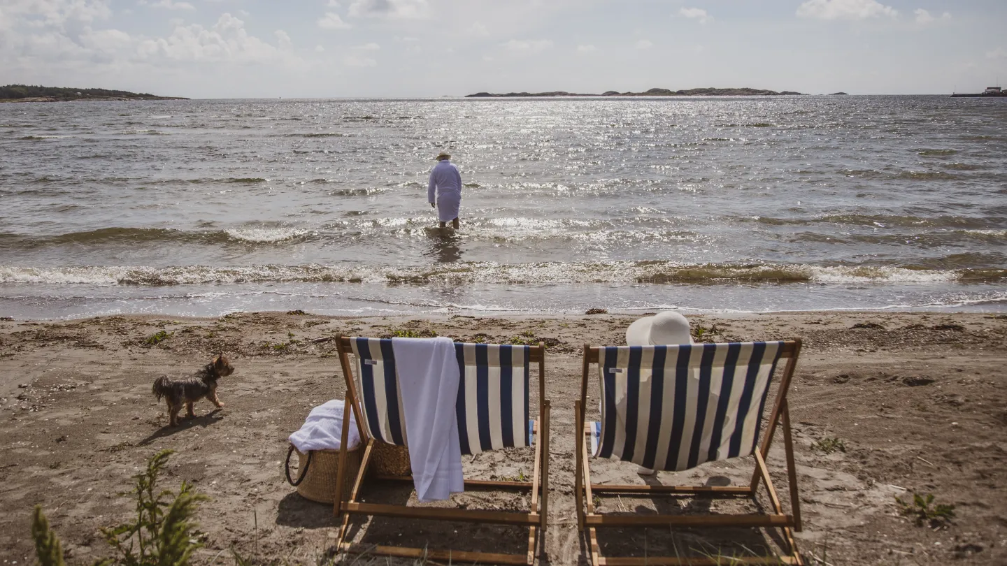 A man walking in the water at the beach. Two beach chairs in the front.