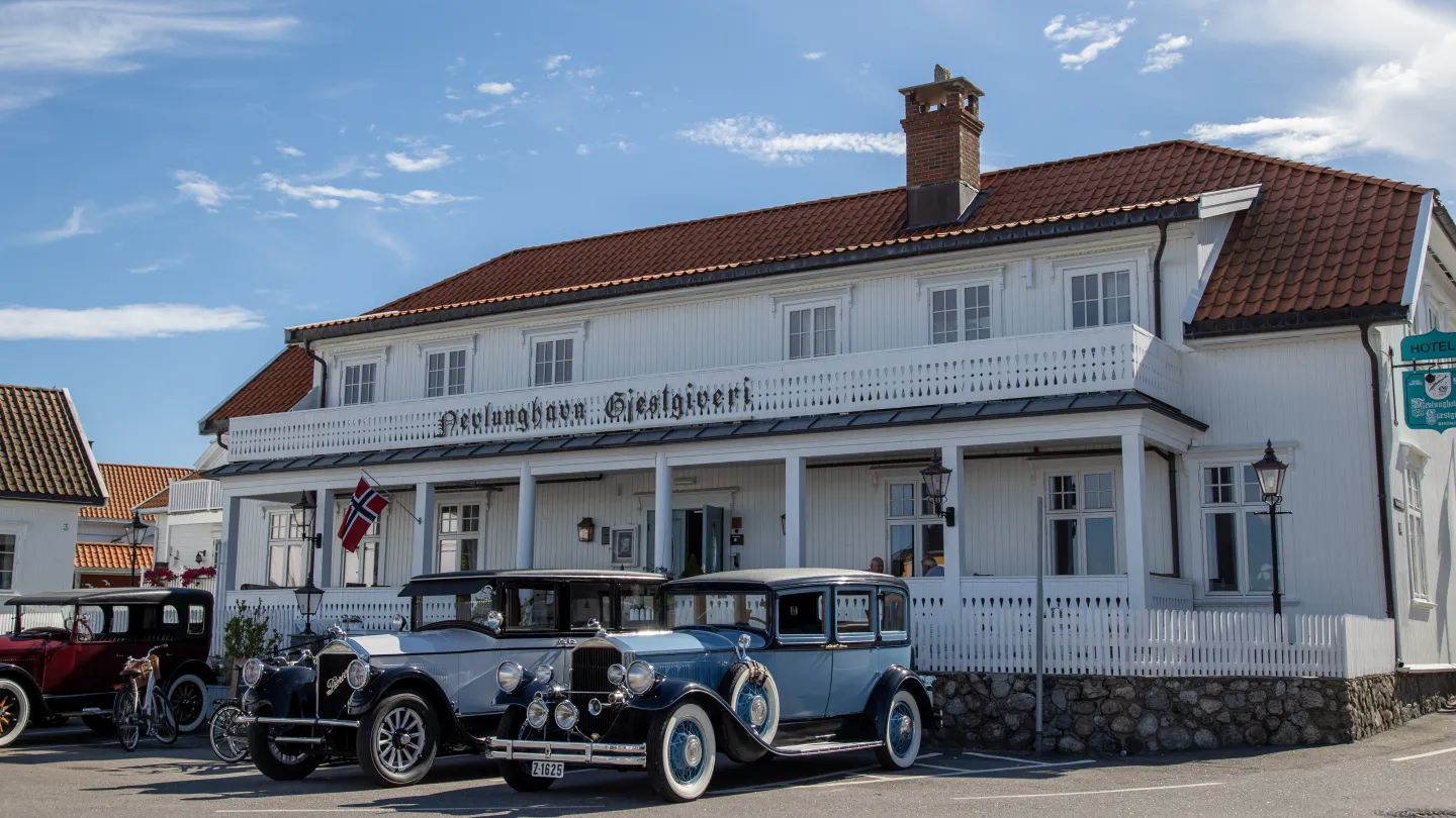 The exterior of Nevlunghavn Gjestgiveri with antique cars parked in the front