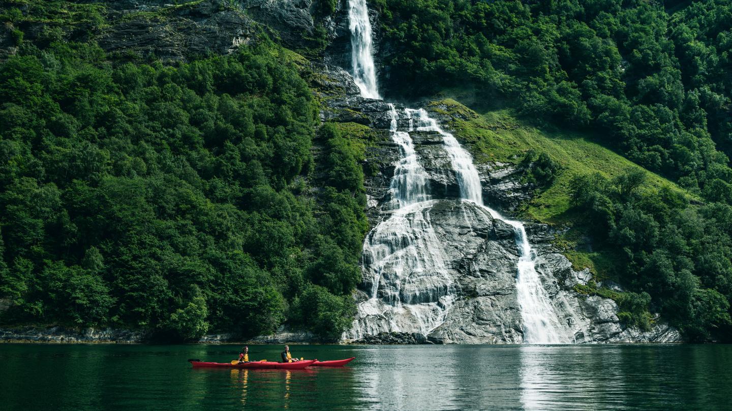 People in kayaks in front of a waterfall on the Geiranger fjord