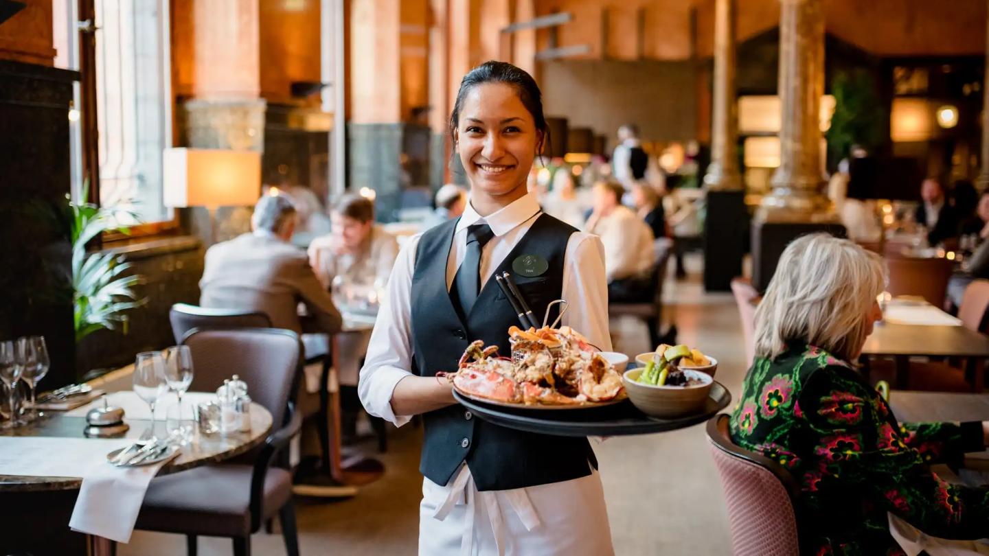 A smiling server with a tray of food in the restaurant of Opus 16