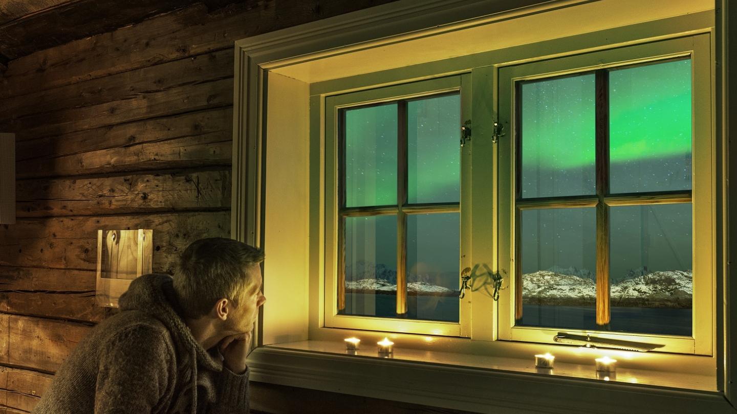 A man looking out on the northern lights from his room at Svinøya Rorbuer