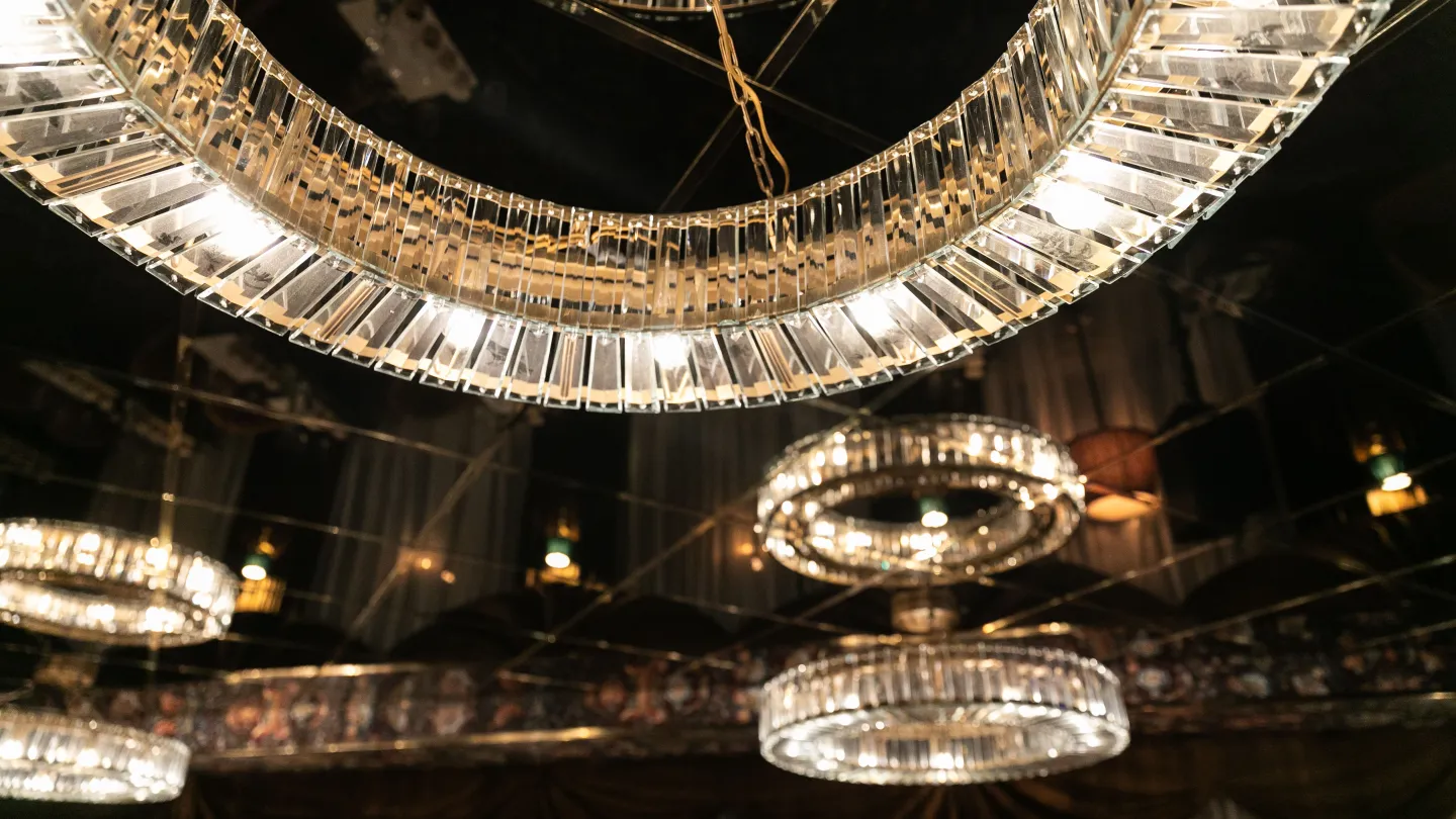 A ceiling detail at Charmante Skostredet Hôtel. Shallow chandeliers made of glass in front of a reflective black ceiling.